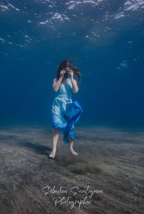 a model in a blue dress is standing in the water during an underwater photoshoot.