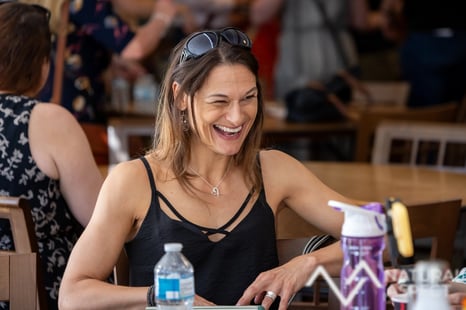 Lady laughing sitting at a table she has sunglasses on her head