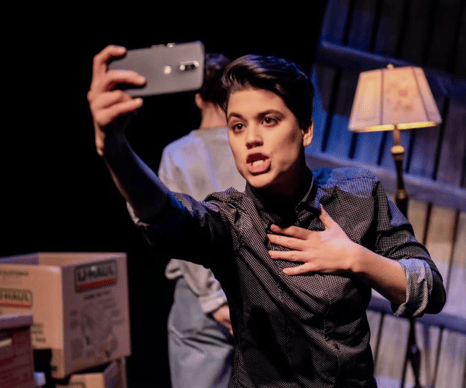 A young person with short hair holds their phone out to record a video of themselves talking