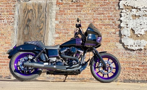 black motorcycle with purple pinstripping parked in front of a old brick wall
