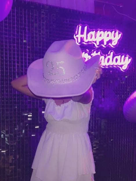 Jamilla with her 25th cow girl hat in front of the Happy Birthday neon sign at her party in Cleveland.