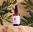 A dropper bottle of Souaad's argan oil set on a sandstone in front of lush green leaves