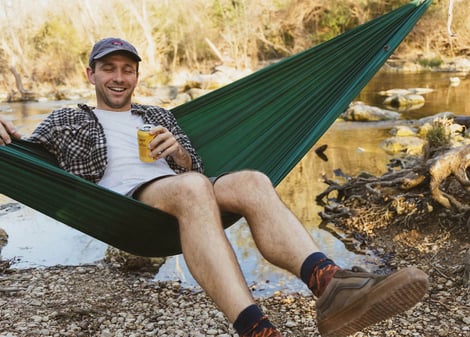 a man sitting in a hammock with a beer