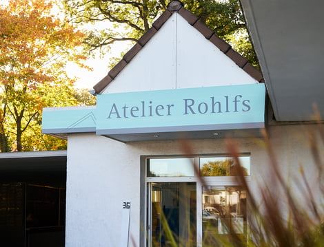 EIne außenaufnahme von einem Gebäude mit Bäumen im Hintergrund auf einem Schild steht Atelier Rohlfs