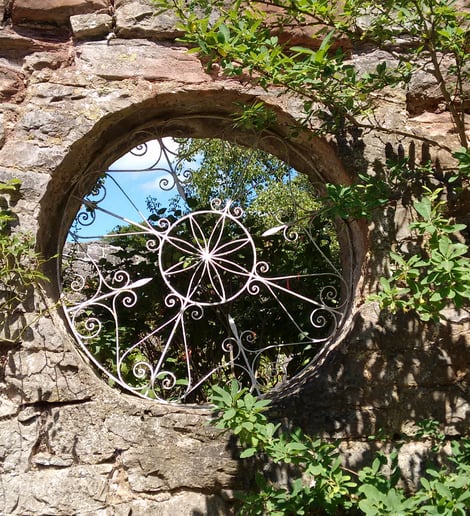 Picture of a stone wall with round opening and wrought iron design inside