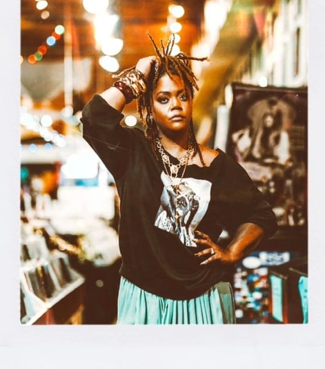 Keri Elle -woman in a skirt and graphic tee is standing in a record store captured by Taye Rose