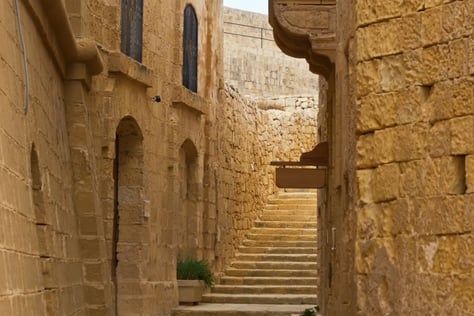 A cat sitting on a stone wall next to a staircase in Gozo's Citadel.