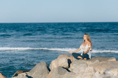 woman meditating on top of a rock near the ocean to relax her mind and be mindful