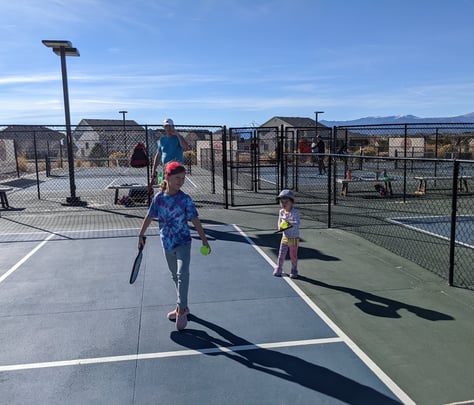 Kids and coach playing pickleball on outdoor courts, promoting family-friendly Smart Dinker training
