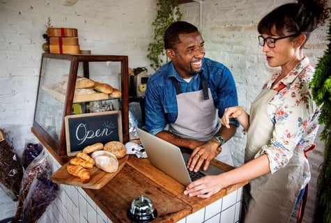 Two small business owners standing behind a counter serving baked goods to customers