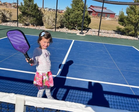 Young girl smiling on a pickleball court holding a paddle during a Smart Dinker kids session.