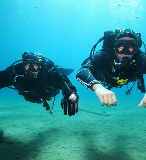 two scuba divers in full bodysuits and diving gear
