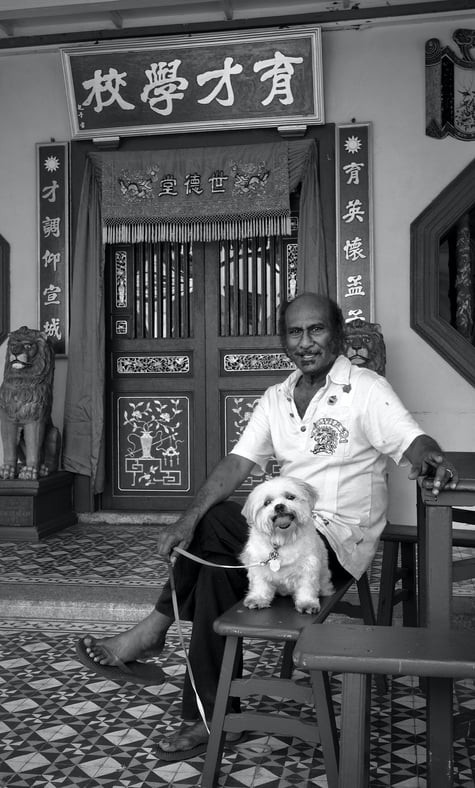 An Indian man and his dog sit outside a temple in Penang by photographer Peter Pickering