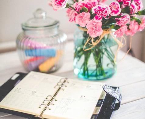 Agenda ouvert à côté d'un vase de fleurs fraîches, symbolisant une organisation soignée et la planification attentive des ses