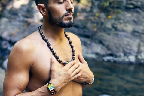 an in deep meditation wearing necklace and blue denim shorts standing on rocky shore during daytime