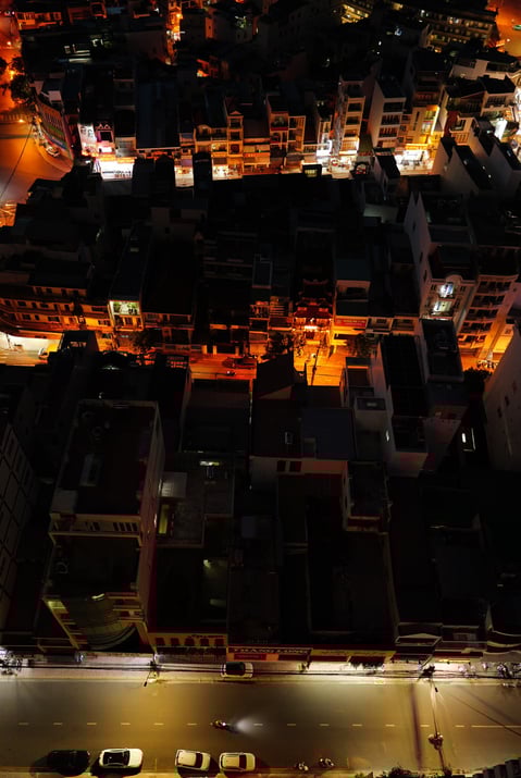 a city street scene by night with warm lights & with cars parked on the street - by ACAT PHOTOS
