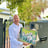 A man in a white shirt stands at his front gate holding a painting of pigs