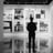 a man in a suit and hat standing in front of a wall with pictures of architectural art prints