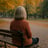 Older woman siting on a bench in the park in the fall