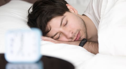 Young man sleeping next to alarm clock wearing smart wristband