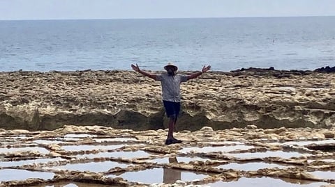 A man stands on the sea shore with his arms out wide. 