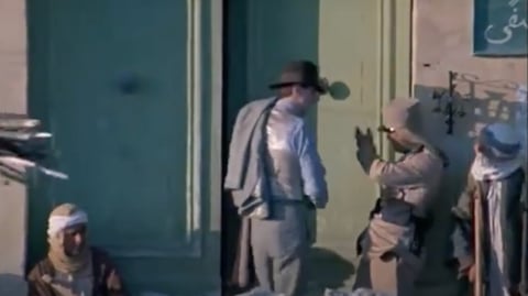 A man in a hat talks to a solider outside a building. 