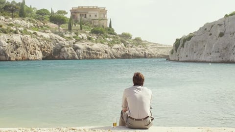 A man sitting on the beach overlooking a body of water.