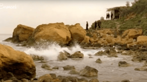 A group of people standing on rocks near a body of water.