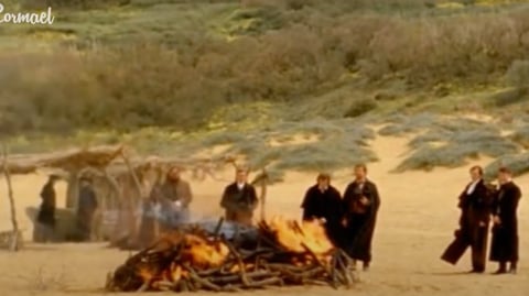 A group of people standing around a bonfire on a beach.