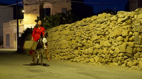 A woman riding a horse alongside a stone wall.