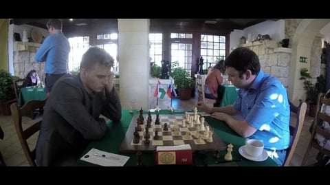 two men playing chess in a room with people.