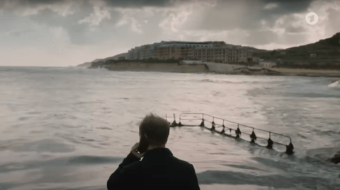 A man stands by a harbour, looking out to sea.