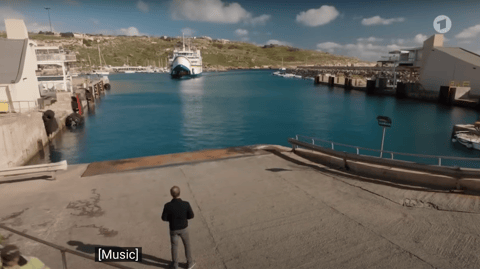 A man stands on a dock as a large ferry approaches.