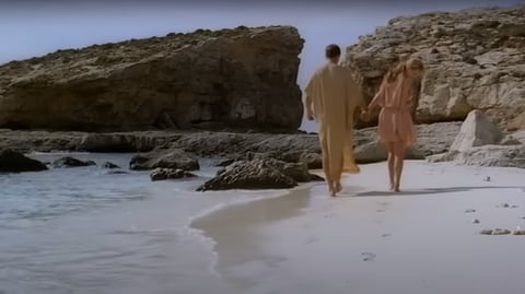 A man and woman walk along a beach.