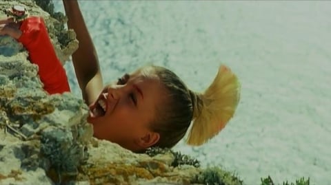 A woman with a blonde mohawk dangles from a cliff edge.