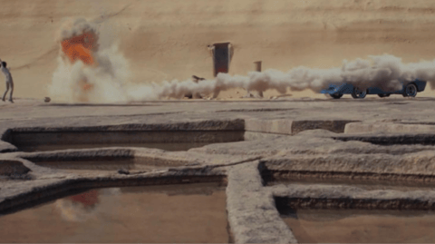 A man standing in front of a limestone cliff by a car covered by smoke.