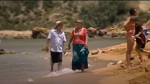 A man and woman walk along the shoreline of a sandy beach.