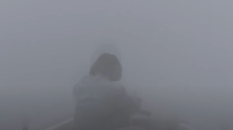 A man in a small wooden dinghy, surrounded by fog.