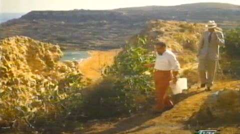 2 men on a cliff overlooking a beach.