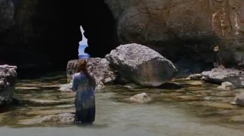 A woman stands in water amongst rocks.