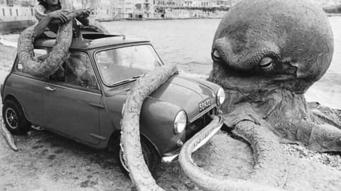 A 1960s mini parked on beach next to a giant octopus.