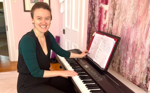 Ellen, a white woman, sits at the piano and smiles at the camera