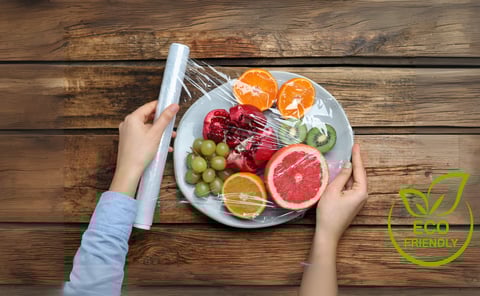 Hands wrapping fresh fruit on a plate with plant-based, eco-friendly food wrap over a rustic wooden