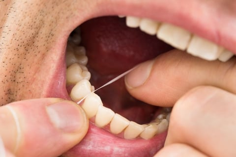 a man cleaning his teeth using dental floss