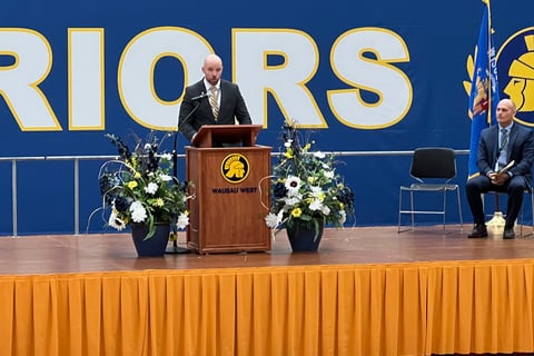 a man standing at a podium with a microphone and a woman sitting at a podium