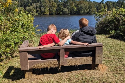 3 kids sitting on a bench in front of a lake