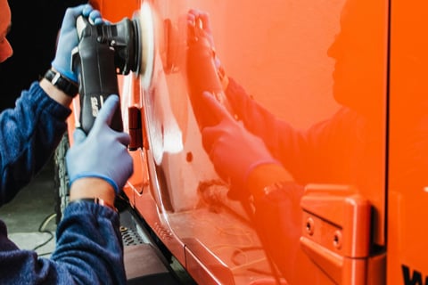 a man in a blue jacket and gloves is buffing a car at fix collision center