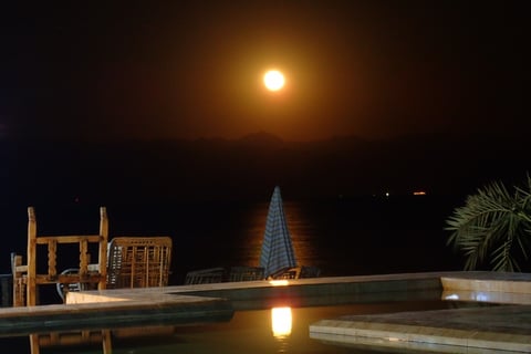 a full moon in the sky reflecting in the  swimming pool in front of  the sea