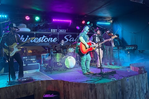 5-man band playing on stage with acoustic and electric guitars, fiddle, and drums