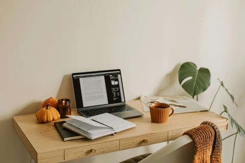 Cozy living: Fall-themed desk with pumpkin decor, lit candle, mug, and warm seasonal accents.